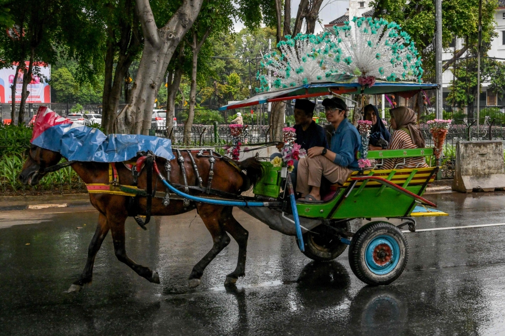 A horse-drawn carriage driver takes passengers for a ride around the National Monument (Monas) park in Jakarta on January 28, 2025. (Photo by Bay Ismoyo / AFP) 