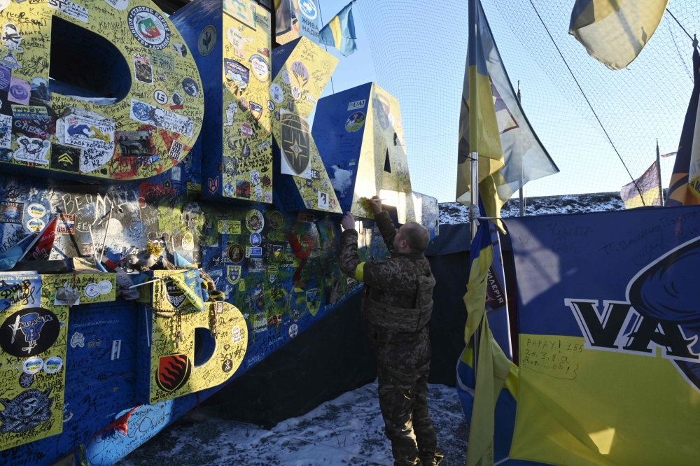 A Ukrainian serviceman leaves a message as he visits the sign indicating the entrance to the Donetsk region, covered by Ukrainian brigades flags and covered with a net to protect it against damages and drones, on February 21, 2025, amid the Russian invasion of Ukraine. (Photo by Genya SAVILOV / AFP)
 