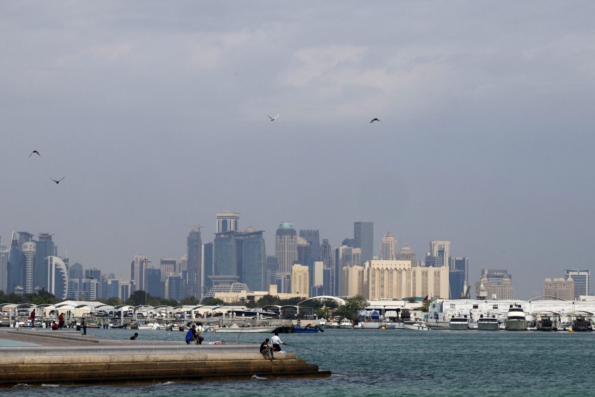 High-rise buildings of the Doha skyline are pictured before men fishing with rods off a pier in the city's harbour on February 17, 2025. (Photo by KARIM JAAFAR / AFP)
