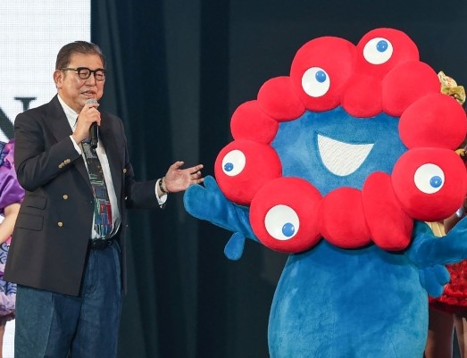 Japan's Prime Minister Shigeru Ishiba stands with Myaku-Myaku, the mascot for the 2025 Osaka World Expo, during a visit to the Tokyo Girls Collection fashion event in the Shibuya district of Tokyo on March 1, 2025. (Photo by Jiji Press / AFP)