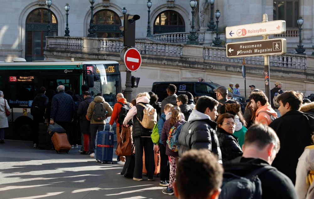 Passengers queue to take a bus from Opera district, in order to reach Paris Charles-de-Gaulle Airport (CDG), as train traffic has been stopped at the Gare du Nord station in Paris on March 7, 2025, following the discovery of a World War II bomb. (Photo by Geoffroy Van Der Hasselt / AFP)