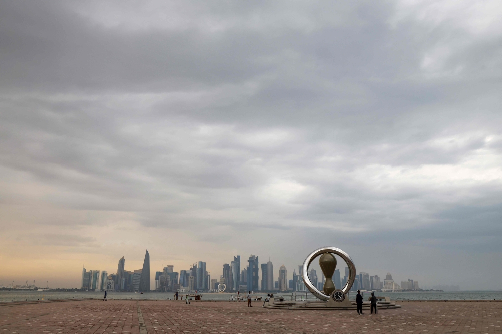 People walk on the Doha waterfront before sunset with the a view of the Qatari capital's skyline in the background on March 9, 2025. (Photo by Karim Jaafar / AFP)