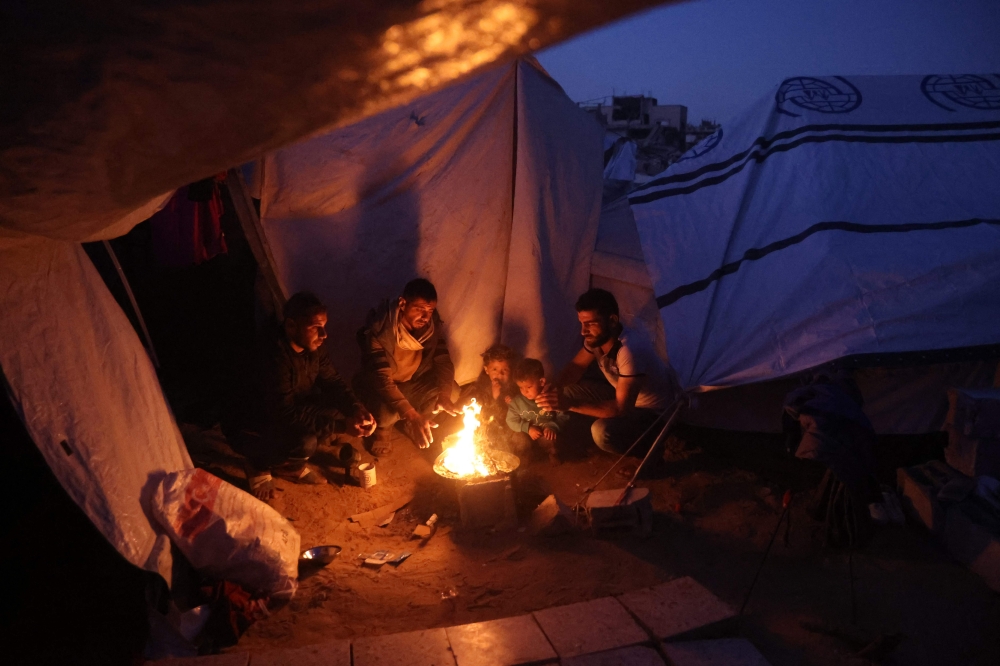 Palestinians gather around a fire to keep warm in Jabalia in the northern Gaza Strip on March 10, 2025. (Photo by Omar Al-Qattaa / AFP)