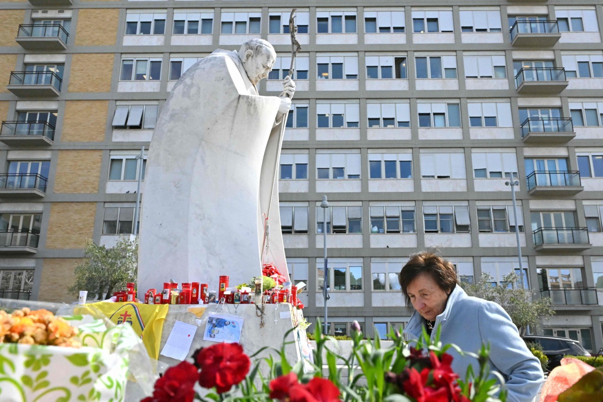 A woman walks next to the statue of John Paul II outside the Gemelli Hospital where Pope Francis is hospitalized in Rome, on March 11, 2025. Photo by Alberto PIZZOLI / AFP