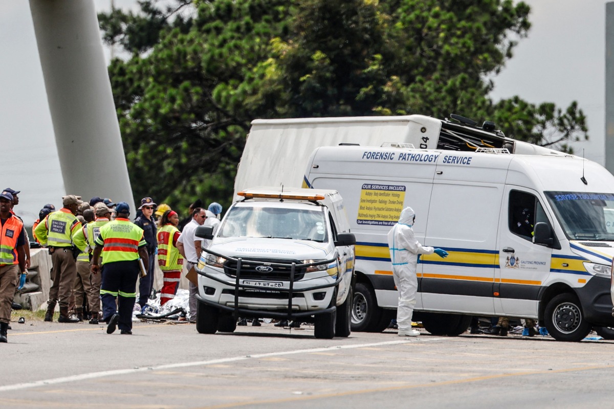 South African emergency services personnel, police and forensic officers stans next to the covered bodies at the scene of a bus accident in Ekurhuleni on March 11, 2025. Photo by WIKUS DE WET / AFP