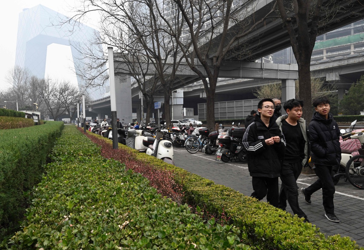 The CCTV Headquarters building (L) is seen as pedestrians walk along the Central Business District (CBD) in Beijing on March 11, 2025. (Photo by ADEK BERRY / AFP)