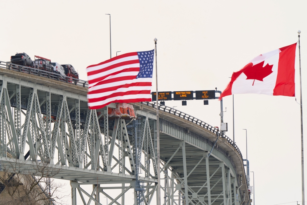 The US and Canadian flags fly on the US side of the St. Clair River near the Bluewater Bridge border crossing on January 29, 2025. (Photo by Geoff Robins / AFP)