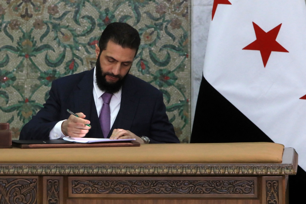 Syria's interim President Ahmad al-Sharaa signs the country's constitutional declaration, which will be enforced throughout a five-year transitional period, at the presidential palace in Damascus on March 13, 2025. (Photo by Bakr Alkasem / AFP)
