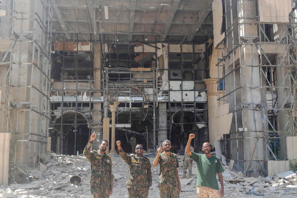 Soldiers of the Sudanese army or affiliated forces pose for a picture while pumping their fists at the damaged presidential palace after recapturing the complex from RSF paramilitaries in Khartoum on March 21, 2025. (Photo by AFP)