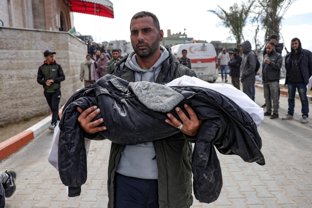 A Palestinian man carries the body of a child killed in an Israeli strike, in the yard of the Indonesian hospital in Beit Lahia in the northern Gaza Strip on March 22, 2025. (Photoby Bashar Taleb / AFP)