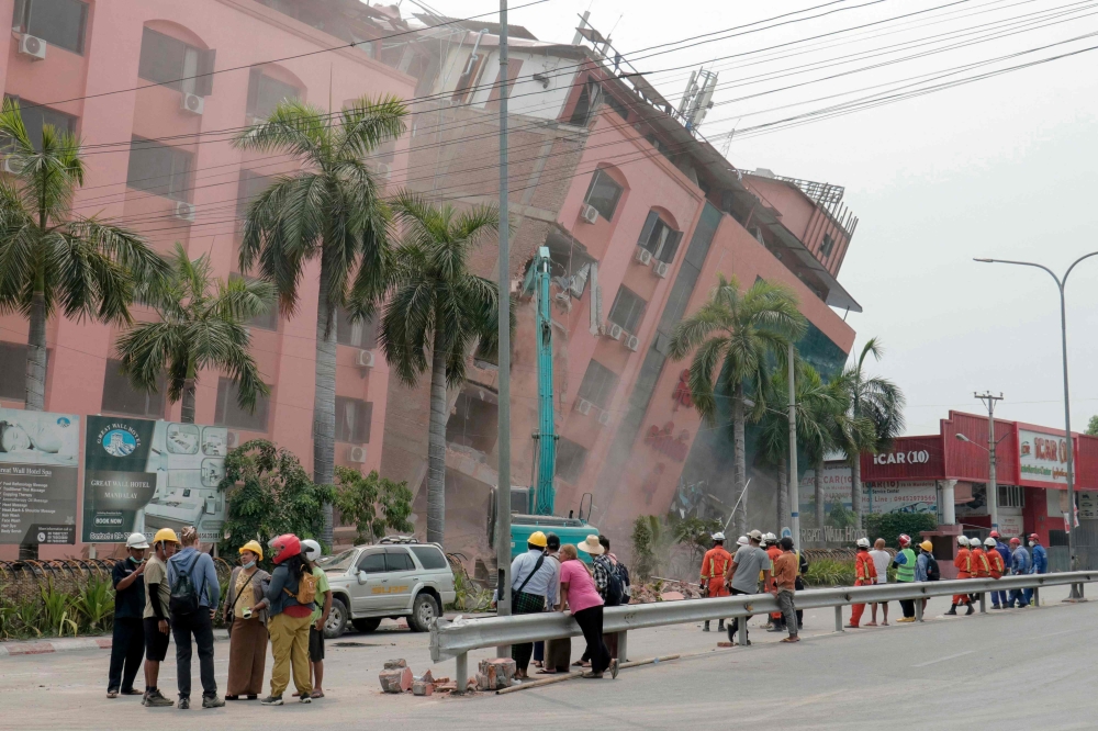 Rescue workers stand on the street next to a collapsed building in Mandalay on April 5, 2025, following the March 28 earthquake. (Photo by Zaw Htun / AFP)